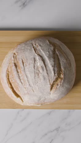 Vertical-Video-Overhead-Shot-Of-Freshly-Baked-Loaf-Of-Bread-Being-Picked-Up-From-Wooden-Board