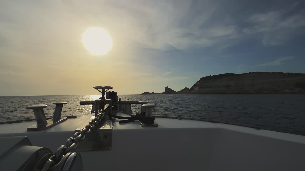 perspectiva desde la proa del barco de vela con sol brillante en frente y acantilados de la isla de córcega y faro de capo pertusato en el fondo, francia-1