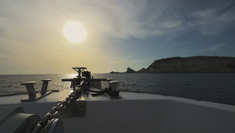 Perspective-from-sailing-boat-bow-with-shining-sun-in-front-and-Corsica-island-cliffs-and-Capo-Pertusato-lighthouse-in-background,-France-1