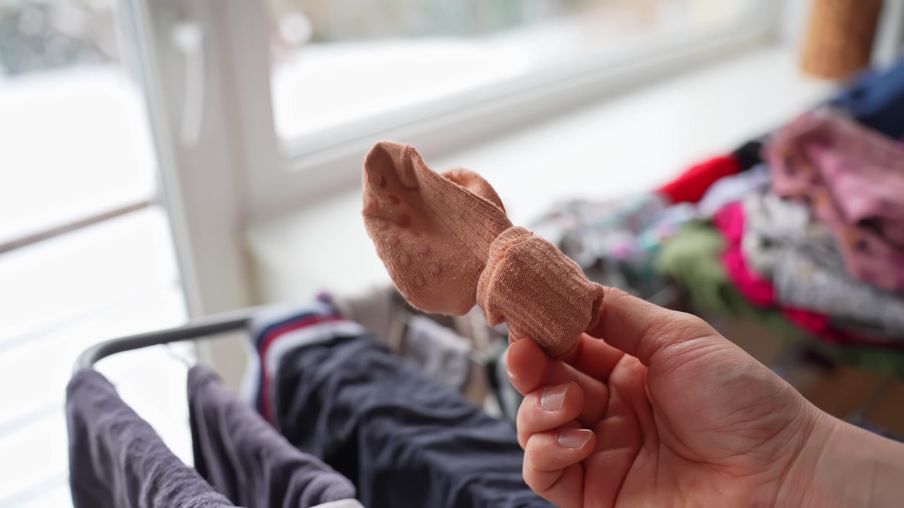 Hand holds and tosses a small sock above a laundry rack in super slow motion by a bright window. Cozy home chore, fabric floating, indoor lifestyle b-roll.