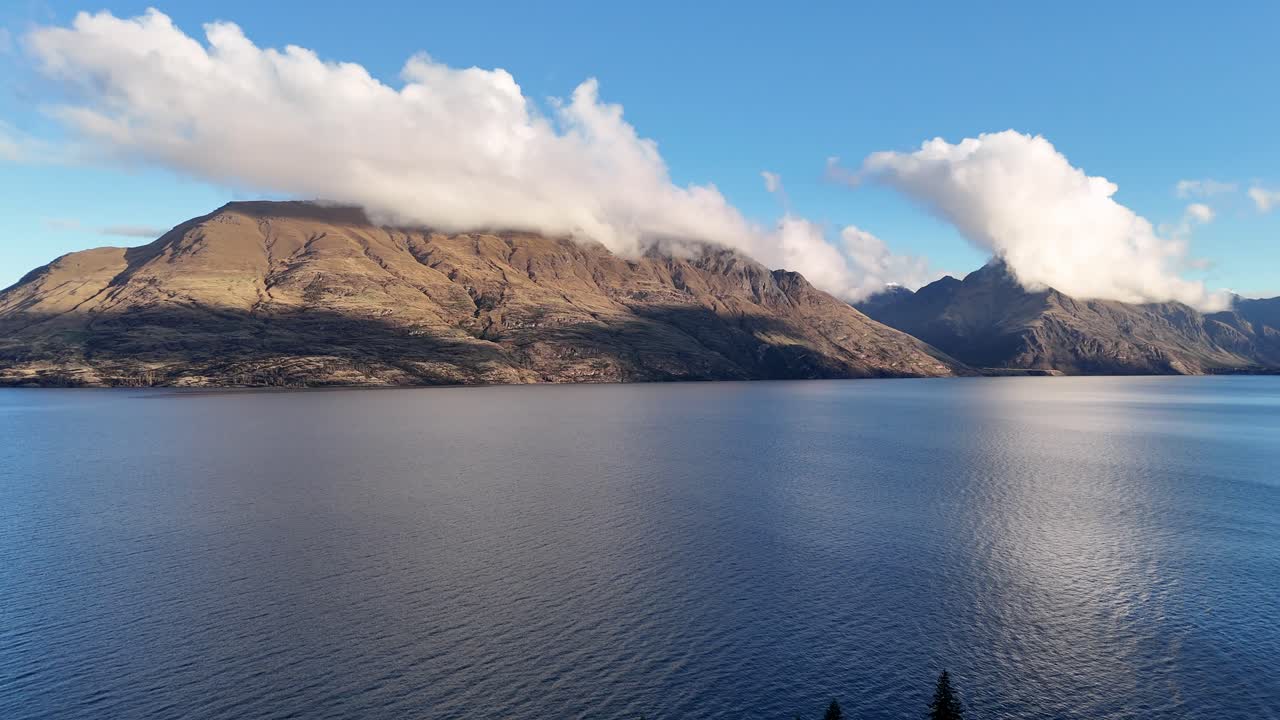 A tranquil lake reflects surrounding mountains under a clear blue sky, captured in Queenstown, New Zealand