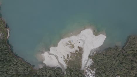 Sandy-coast-surrounded-by-dense-forestry-area-near-mountain-lake-in-Norway,-aerial-top-down-shot