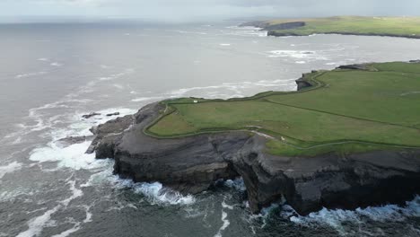 kilkee coastline with grassy cliffs and waves crashing against the shore, aerial view