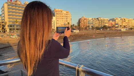 tourist taking pictures of las canteras beach in gran canaria, spain, at sunset. slow motion