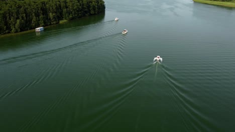 Several-motor-boats-driving-on-a-lake-next-to-a-forest-in-Brandenburg,-Germany