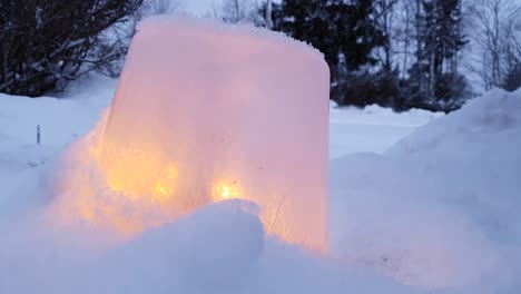 Candle-in-ice-lantern-with-snowflakes-falling-slowly-in-winter-background