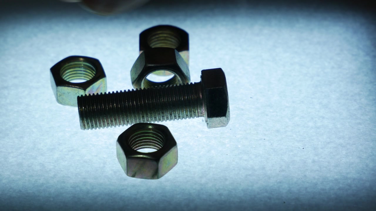 Mão Colocando Porcas Sextavadas de Metal em Torno de um Parafuso em Superfície Texturizada.