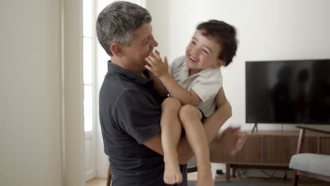 padre alegre sosteniendo a su hijo pequeño en sus brazos y acurrucándolo