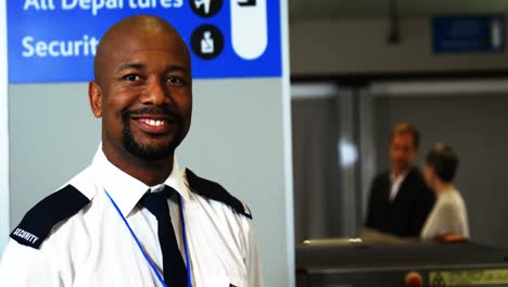 Smiling-security-staff-holding-metal-detector-standing-at-airport