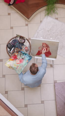 artist draws woman face in home studio. art creator touches canvas with brush imagining female model portrait in studio. man rests with creative hobby