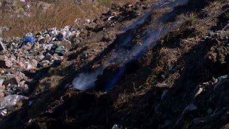 slow motion, handheld view of smoke and flames emerging from the garbage at a dumping site