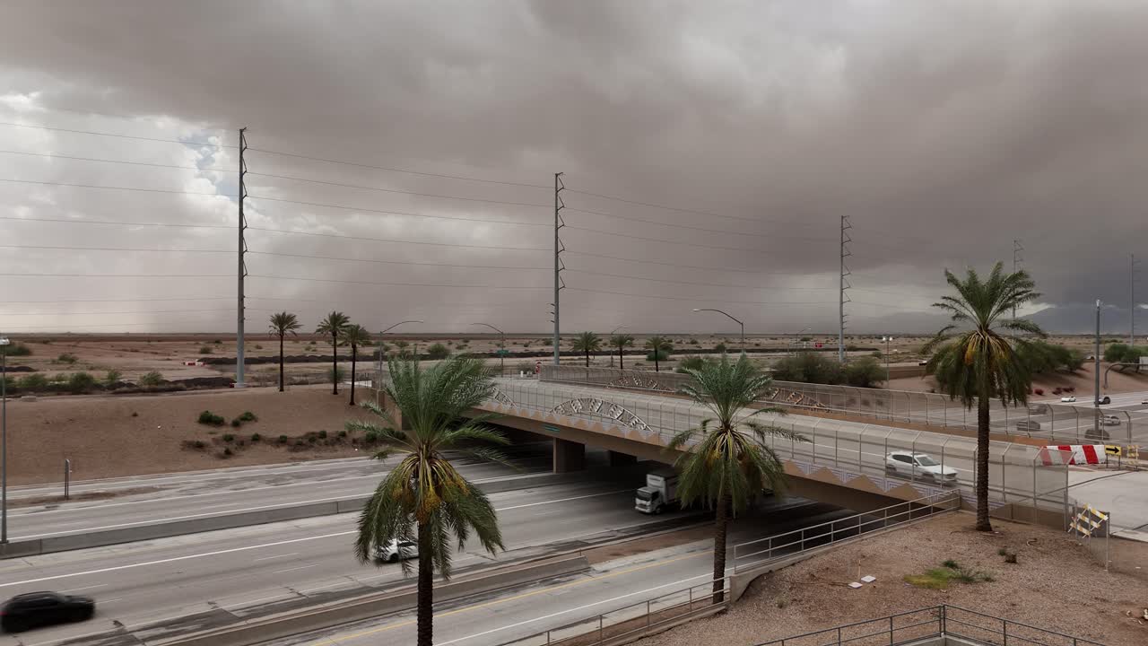 Static Shot of Highway 202 in chandler Arizona with Huge Dust Storm in the background, windy day, palm trees blowing in foreground, cars driving on highway