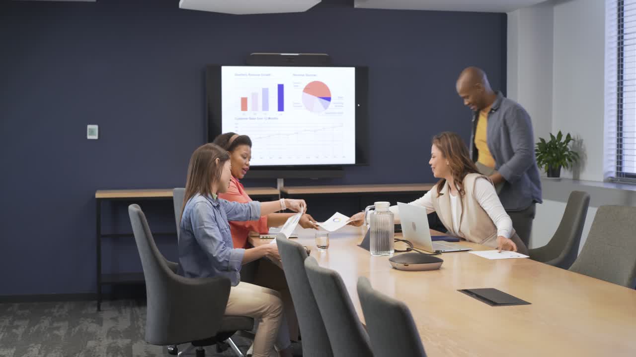 Diverse coworkers in business attire entering conference room, pointing at charts, reviewing data