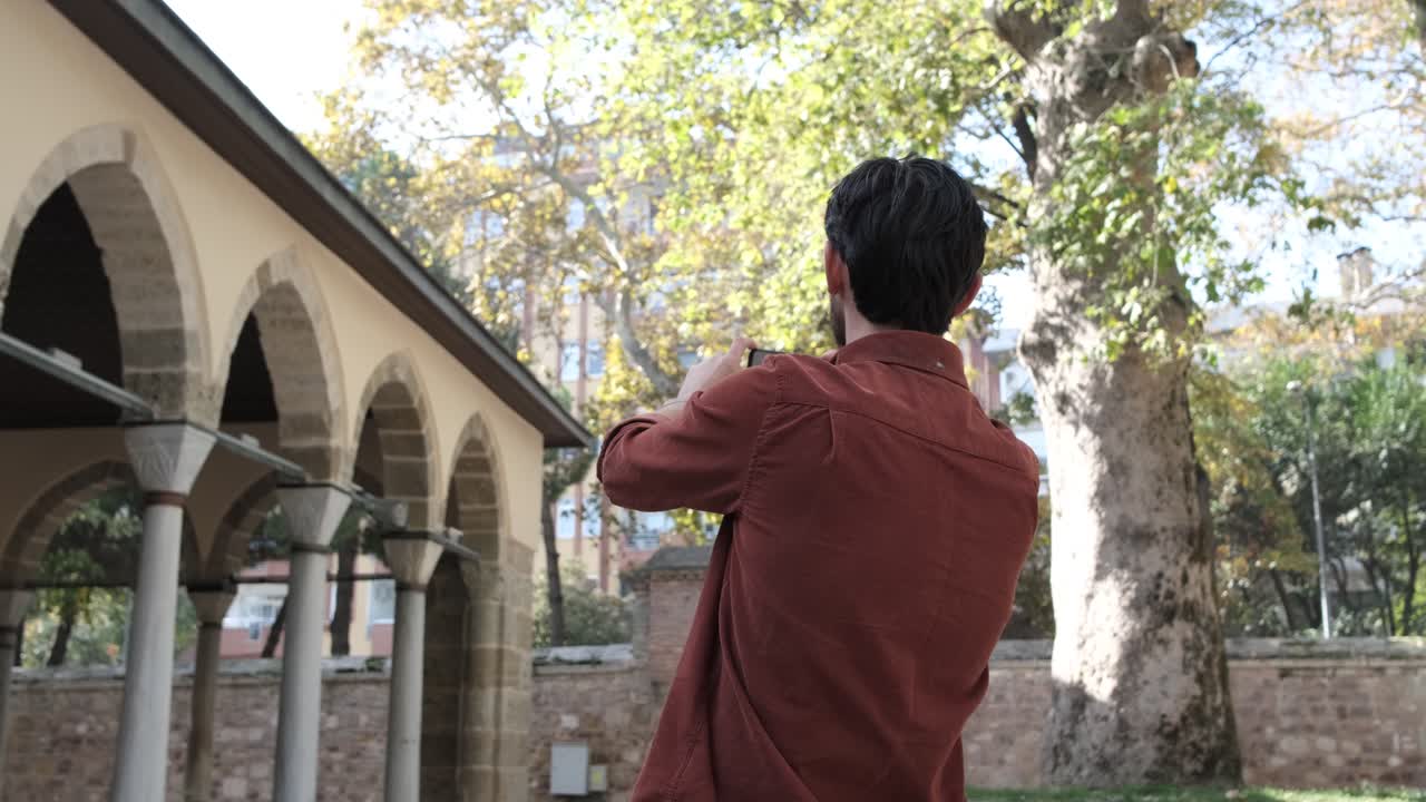 Side view of a young bearded man taking a photo of the mosque, the mosque is the place where Muslims pray