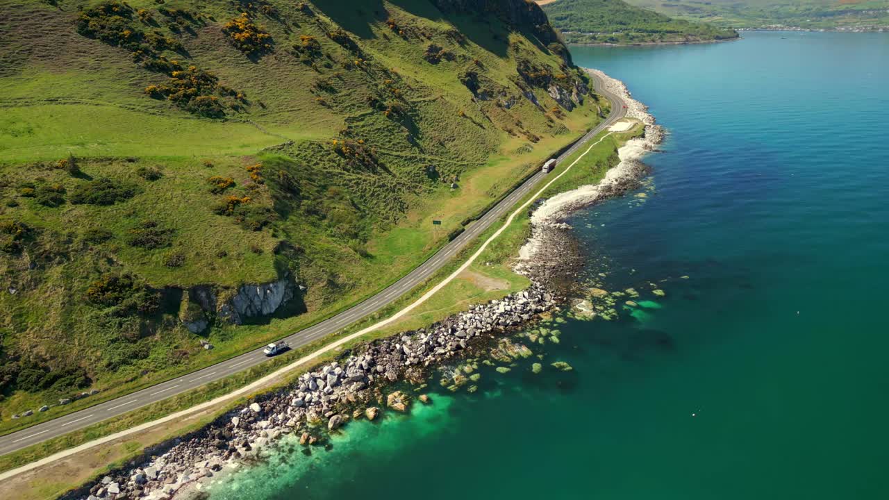 Left-to-right travelling aerial video of the Causeway Coastal Route in County Antrim, Northern Ireland, UK, on a bright and sunny day. Cars pass below. Filmed in 4K, 60FPS and with Rec709 color.
