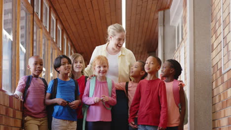 female teacher walking with group of diverse students in school hallway, smiling together