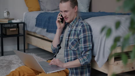 man working on laptop while on phone call in bedroom