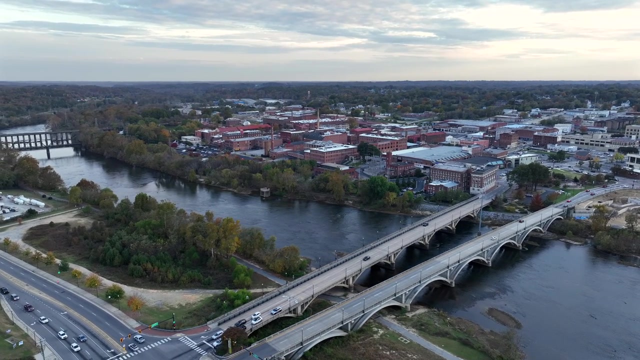 Scena al crepuscolo in una città americana con fiume e ponte. Auto che guidano su una strada all'incrocio e attraversano il ponte. Edifici storici della città con facciata in mattoni rossi. Giorno autunnale di sera. Veduta aerea