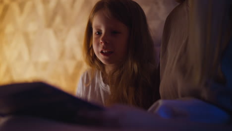 child turns page of fairy tale book reading with mum on bed