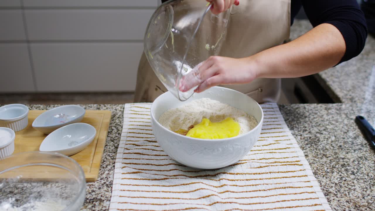 una foto en cámara lenta de una mujer vertiendo calabaza cocida en un cuenco de cerámica con harina.