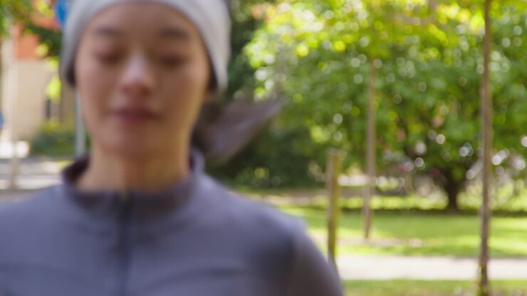 Primo piano di una giovane donna che si allena correndo attraverso un parco cittadino, indossando auricolari wireless