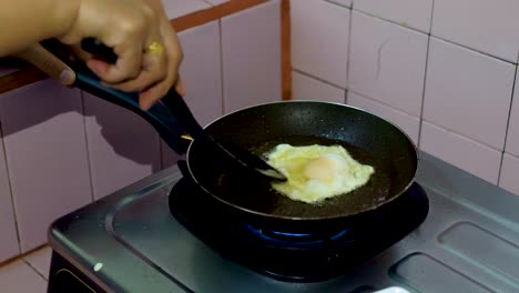 Hands-of-woman-cooking-fried-egg-on-black-pan-in-domestic-kitchen,-close-up-view