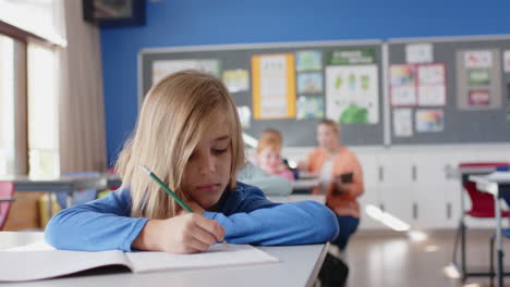 in school, boy holding pencil and resting head on desk in classroom