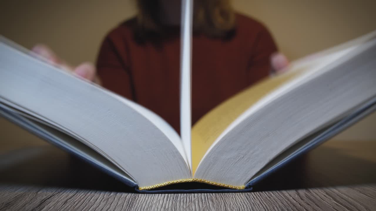 mujer abre un libro sobre una mesa de madera y empieza a leer - cámara lenta