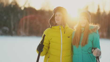 in the winter forest at sunset a man and a woman ski and look around at the beauty of nature and attractions in slow motion.