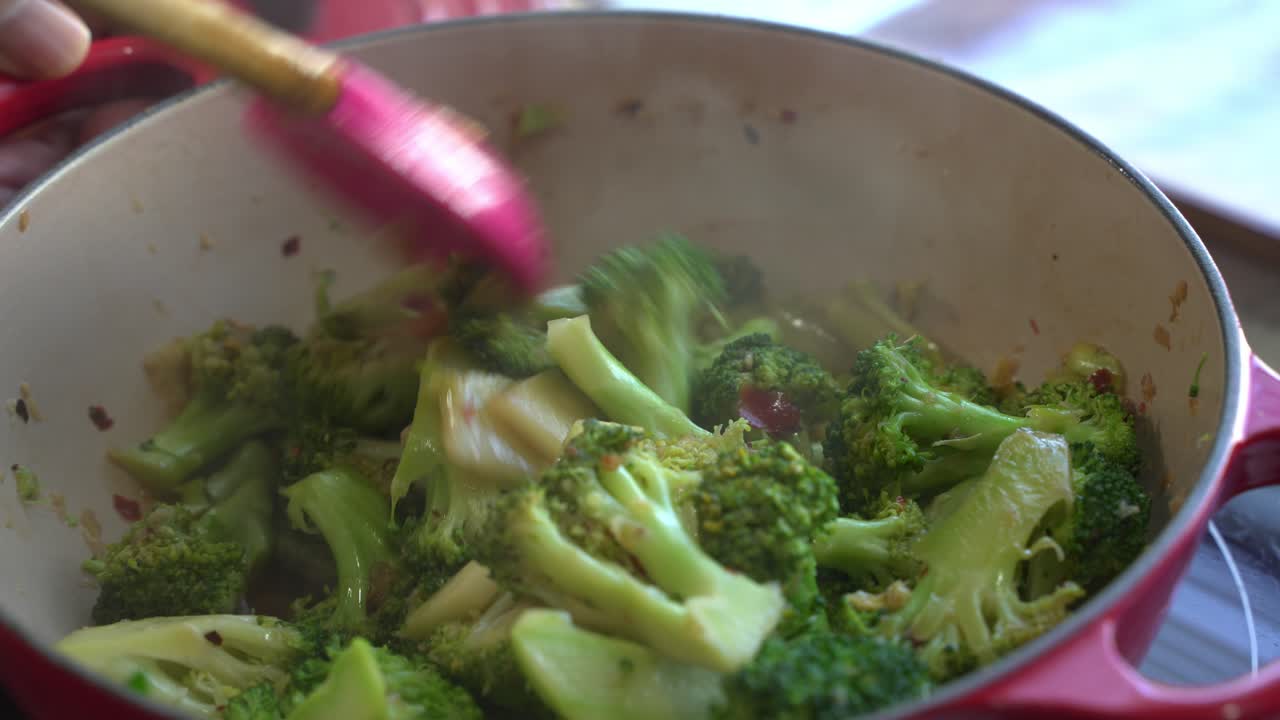 Stir-frying broccoli in a red pot with a pink spatula