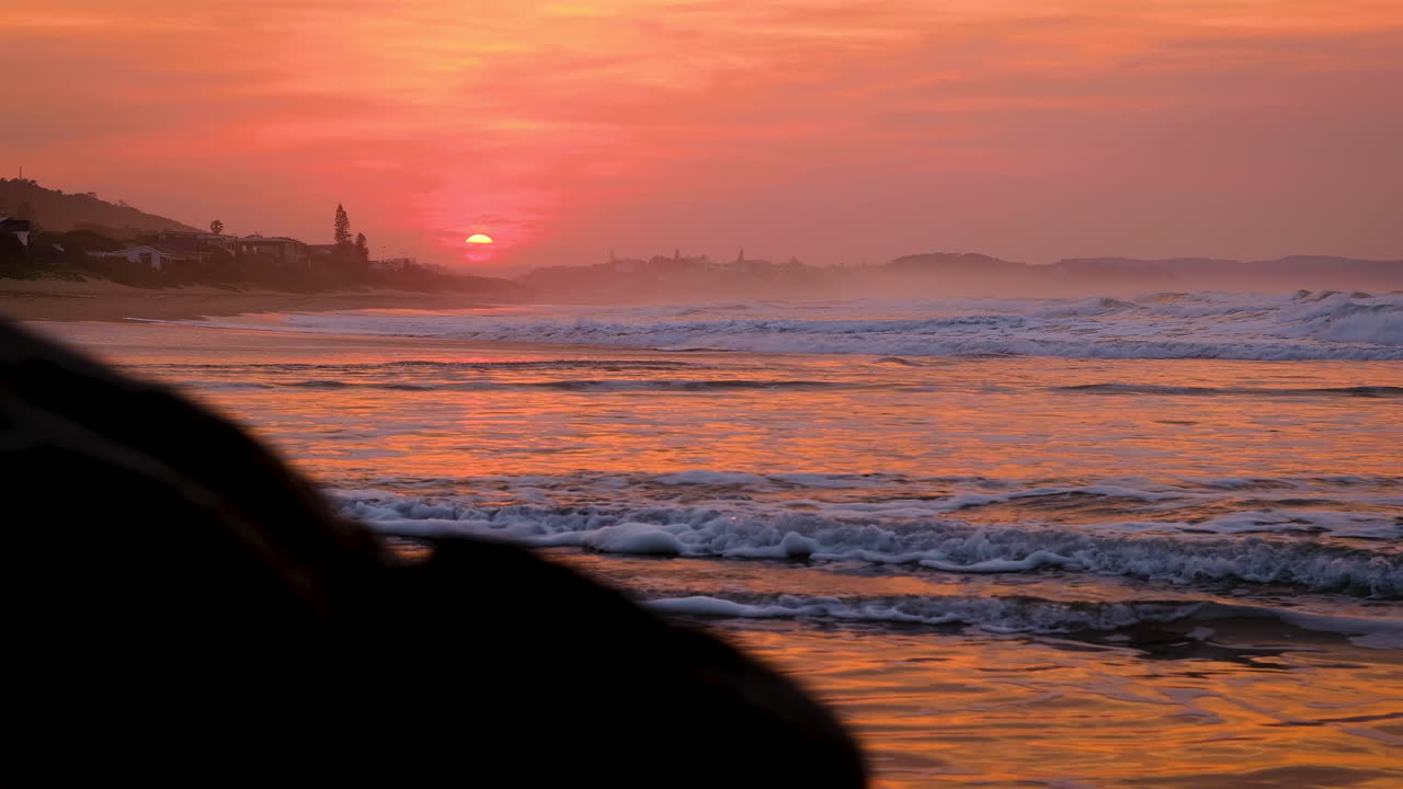 Vibrant sunrise lights sky on fire over beach, yellow orb, low waves crashing