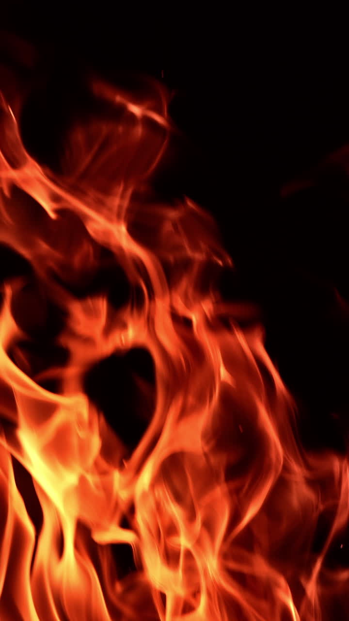 Red fire flames dancing in the darkness. Beautiful hypnotic view of the campfire close up. Vertical video