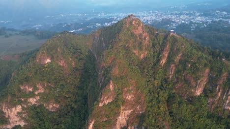 Drone-view-in-Guatemala-flying-in-front-of-a-green-mountain-face-shaped-surrounded-by-volcanos-at-sunrise-in-Atitlan