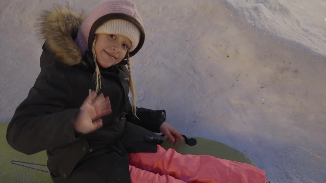 Young Girl Waving While Sitting on a Sled in the Snow