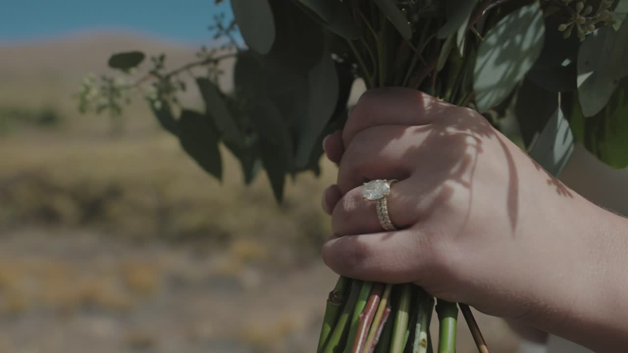 Noiva em câmera lenta segurando flores com seu anel de noivado na natureza.