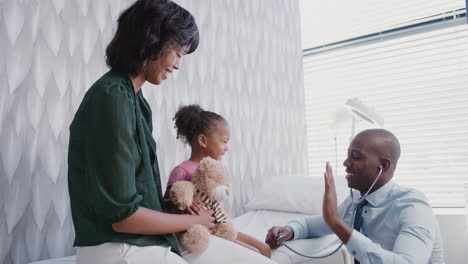male doctor giving girl and her teddy bear medical exam on family consultation in office