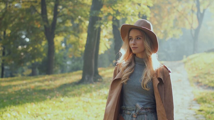 Caucasian woman with blonde hair wearing a coat and hat walking in the park in the morning in autumn