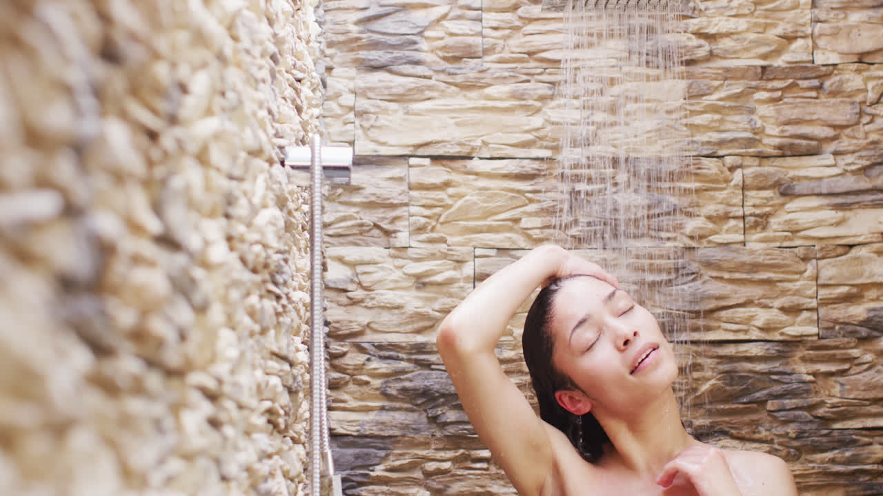 mujer biracial sonriendo y duchándose en el baño