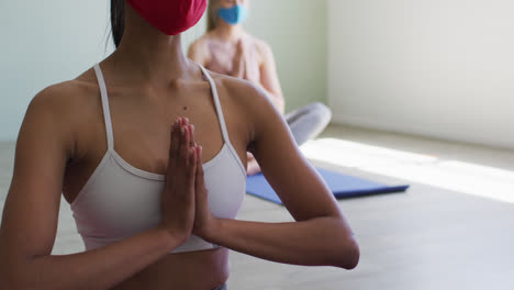 dos mujeres caucásicas en forma que llevan máscara practicando yoga en el estudio de yoga