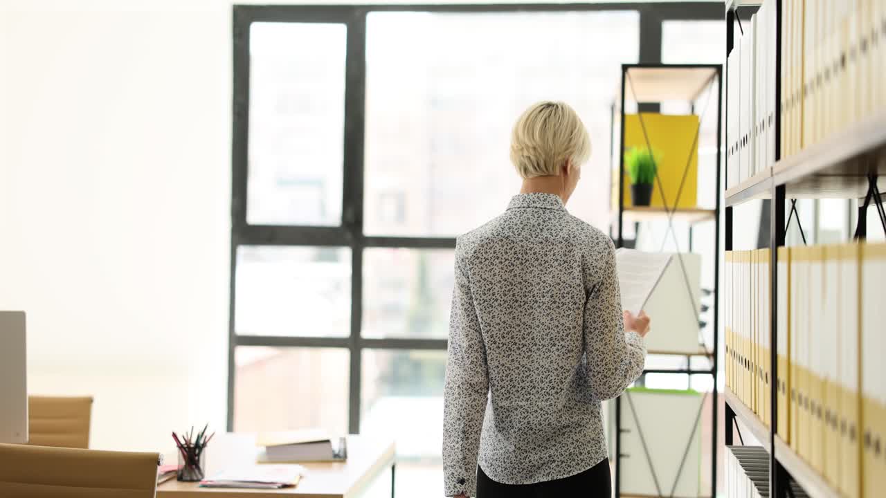 Kvinde står på et kontor og kigger på dokumenter og hylder
