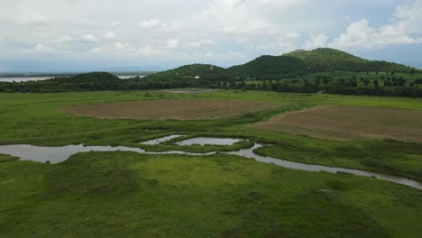 reverse aerial footage of hills covered with trees, a lake, grassland, farmland and the elevated railway in muak klek, saraburi, thailand