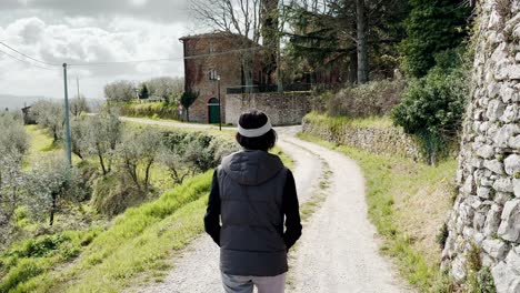 Woman-walking-in-ancient-stone-village-of-Italy-on-sunny-day,-back-view