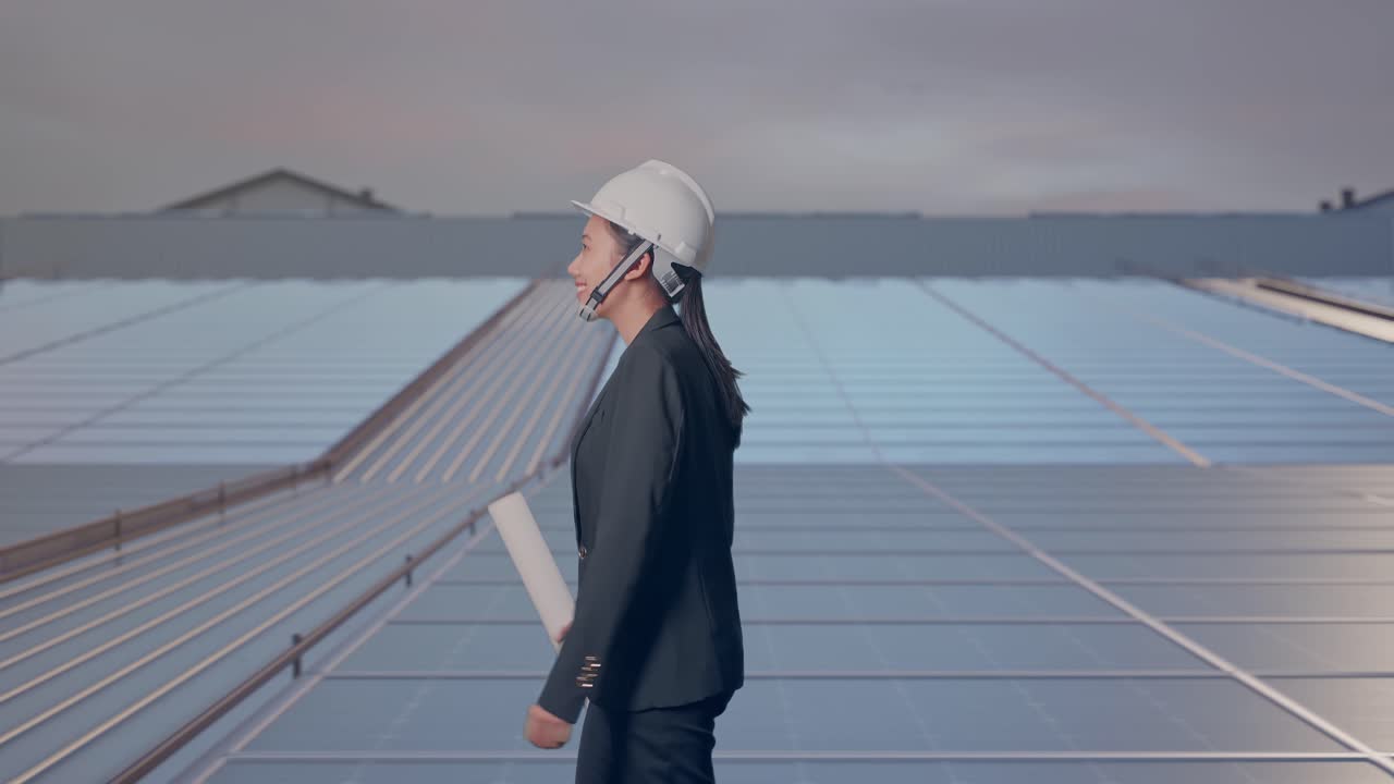 Vista lateral de empresaria asiática sosteniendo un plano mientras camina y observa en paneles solares industriales en la azotea