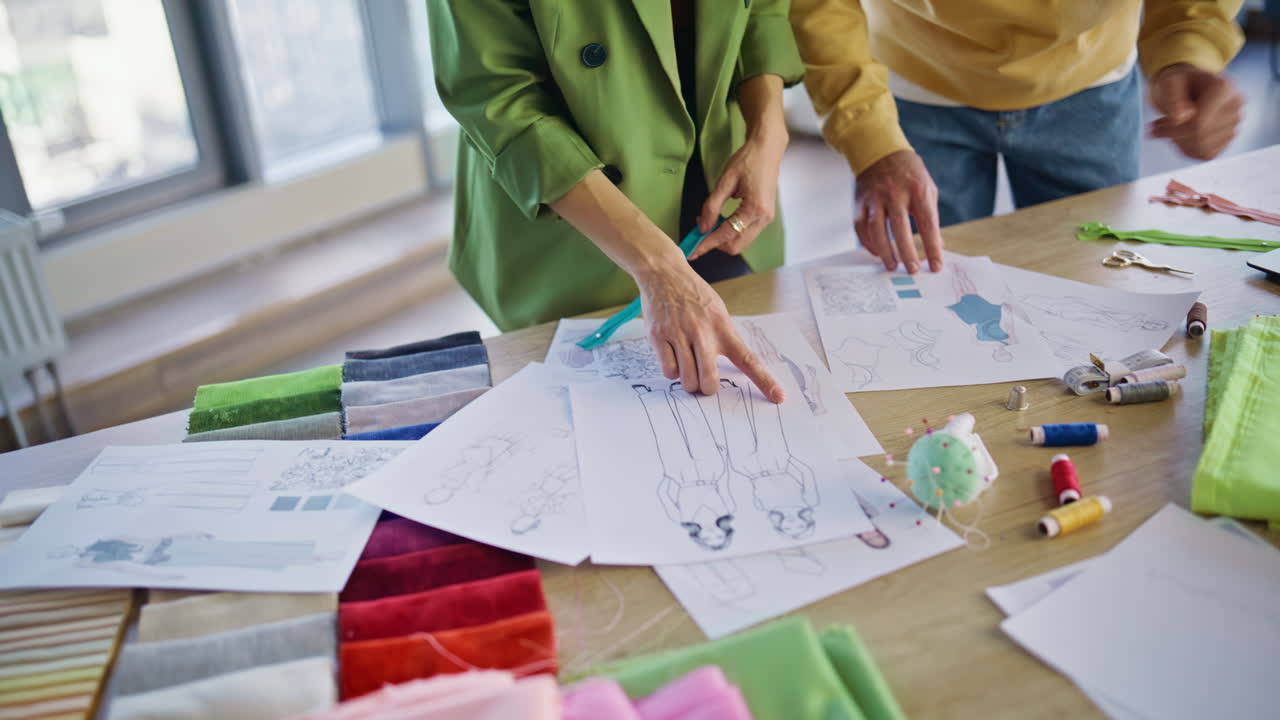 Dressmakers hands working fashion clothing sketches at agency desk closeup