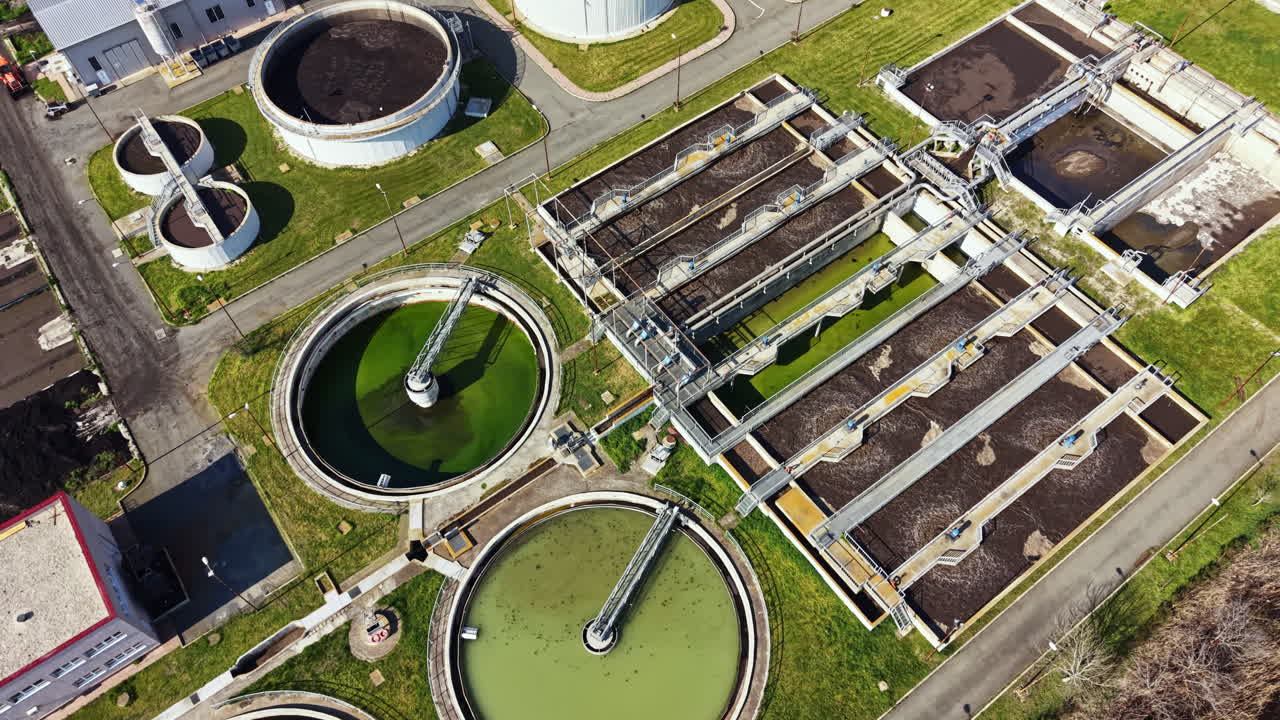Wastewater treatment facility processes water using large tanks and machinery in an urban area during a sunny day