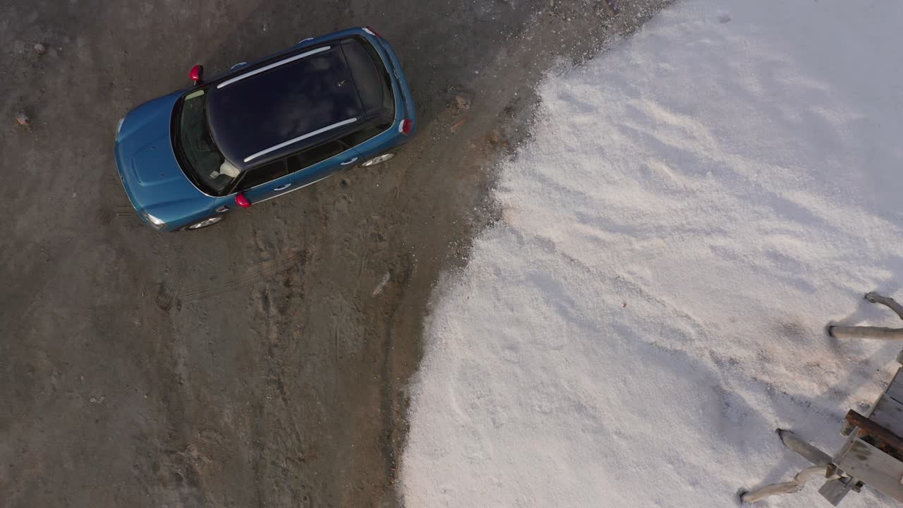 Blue Hatchback Mini Cooper with Red Rear View Mirrors Parked on Dirt next to a Wooden Picnic Bench on Sand, Drone Aerial Birdseye Ascend