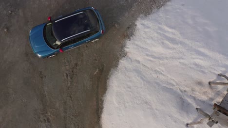 Mini-Cooper-Hatchback-Azul-Con-Espejos-Retrovisores-Rojos-Estacionados-En-La-Tierra-Al-Lado-De-Un-Banco-De-Picnic-De-Madera-En-La-Arena,-Ascenso-Aéreo-Drone-Birdseye