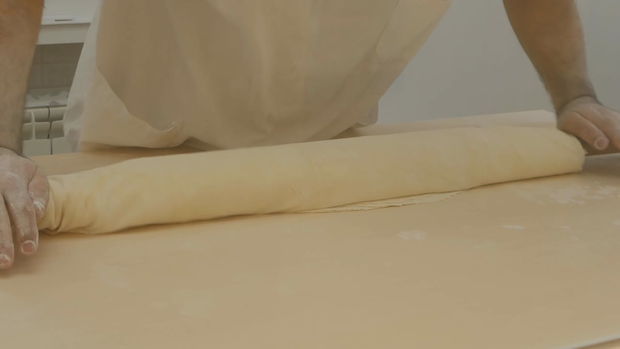 un confitero, un árabe, enrolla las capas de masa en un rodillo y las extiende con la mano. cocinar baklava turca. proceso de preparación de postre nacional