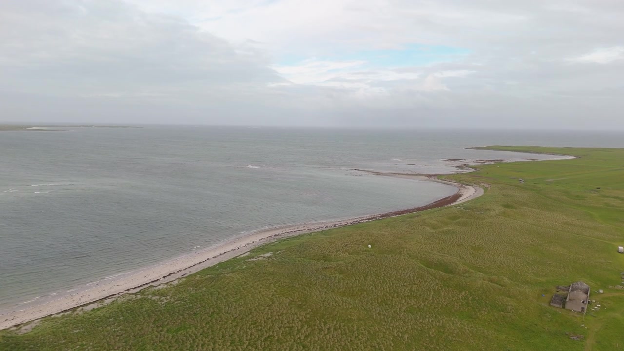 Una ripresa aerea cinematografica in movimento che mostra l'intersezione tra campi di erba verde lussureggiante e acqua calma dell'oceano blu in una giornata nuvolosa. Ideale per contenuti su sostenibilità e viaggi ecologici.