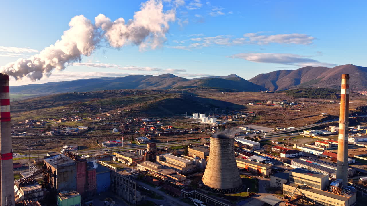 Paesaggio aereo di una centrale elettrica attiva con torri di raffreddamento, gruppi elettrogeni e fumo su uno sfondo montuoso. Impianto di centrale termoelettrica.